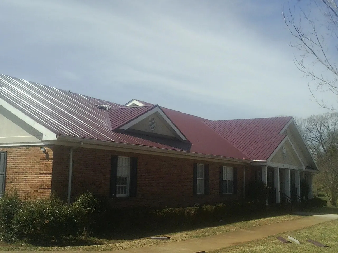 Red metal roof with gabled entries on a long brick building, from a Hail Damage Roof Repair job in Mount Pleasant Mills