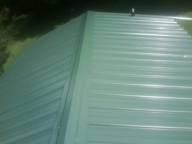 New green metal panels meeting at the ridge of a roof — Flat Roof Repair work by our crew in Mount Pleasant Mills