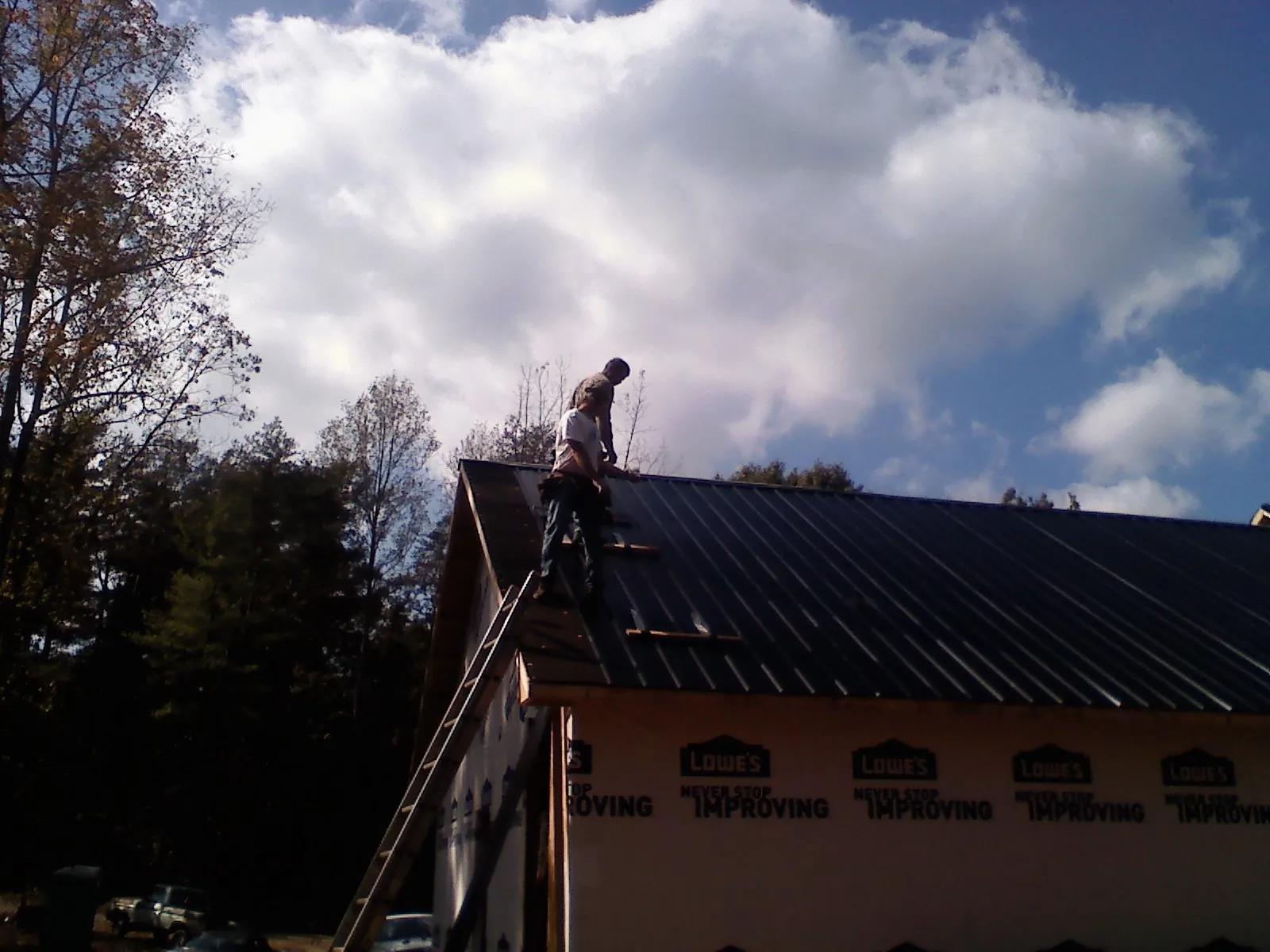 Roofer fastening dark metal panels high against a cloudy sky, from a Roof Inspection job in Mount Pleasant Mills