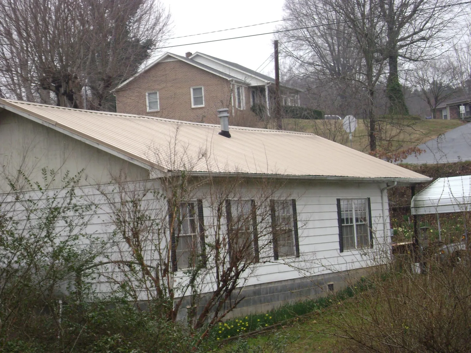 Tan metal roof on a white sided house set into a hillside — Commercial Roofing by Roofing Brothers in Mount Pleasant Mills